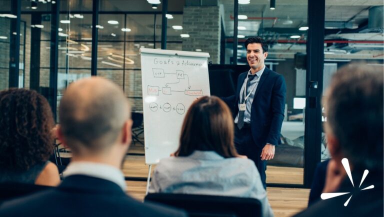 Business leader presenting goals and strategy on a flip chart to a seated team in a modern office, representing IDI leadership development and communication.